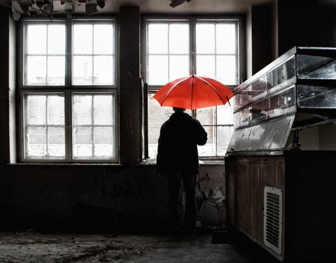 Homem segurando guarda-chuva vermelho aberto dentro de edifício