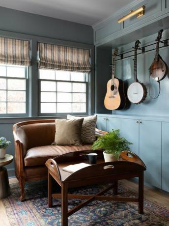 sala de estar, paredes pintadas de azul, sofá de couro marrom, mesa de centro marrom, instrumentos musicais pendurados nas paredes, tapete marroquino