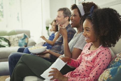 Jovem família multiétnica assistindo filme e comendo pipoca no sofá