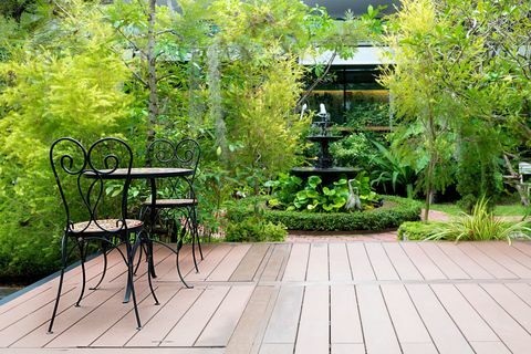 Cadeira preta no pátio de madeira no jardim verde com fonte em casa. Jardim ao ar livre.