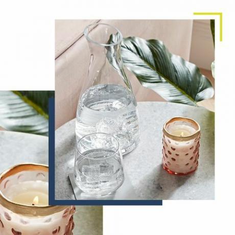 uma vela acesa sobre uma mesa lateral de mármore ao lado de uma jarra de água com copos