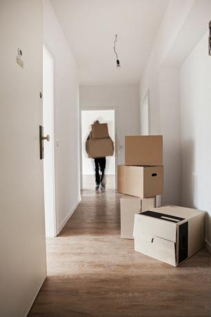 Homem descarregando caixas de papelão no corredor de uma casa nova