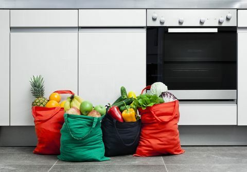 Sacolas reutilizáveis ​​cheias de frutas e legumes em uma cozinha.