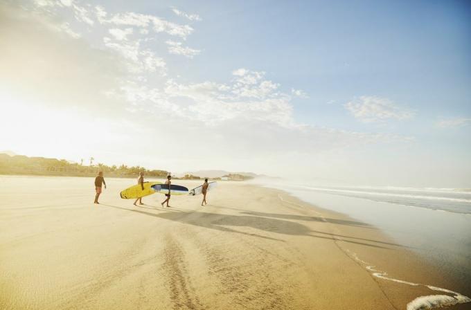 tiro amplo extremo da família carregando pranchas de surf na praia tropical enquanto toma aulas de surf durante as férias