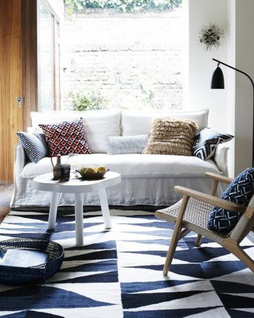 sala de estar, sofá branco e janela de tapete kelim de triângulos azuis atrás de um sofá de linho simples e mesa de centro branca são um pano de fundo perfeito para um tapete azul e branco geométrico e almofadas tonificantes