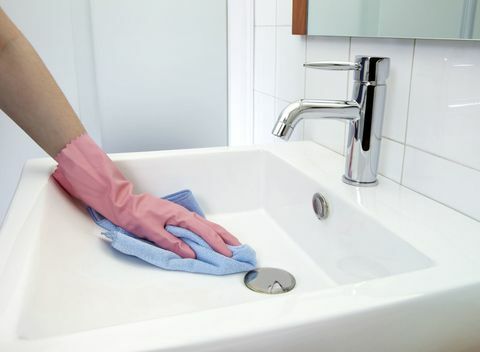 Lavatório de limpeza: A mulher que está limpando o lavatório com pano e luvas de microfibra