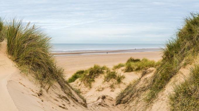 um panorama de várias imagens capturado entre dois picos nas dunas de areia olhando para as pessoas caminhando ao longo da praia de formby perto de liverpool