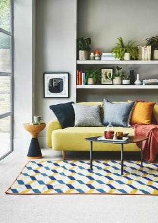 sala de estar, sofá amarelo prateleira branca atrás com um tapete estampado azul e amarelo no chão