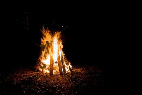 uma fogueira ao ar livre com grandes chamas contidas em tábuas em forma de tenda