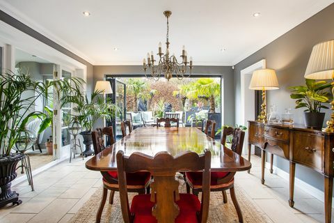 sala de jantar com mesa e cadeiras de madeira escura e bi portas dobráveis ​​para jardim