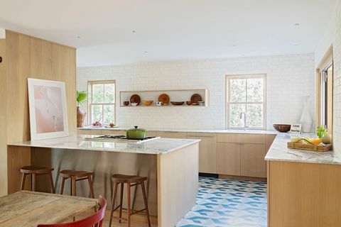 cozinha com armários de madeira, bancada de mármore, azulejos azuis, brancos e cinza, bancos altos de madeira