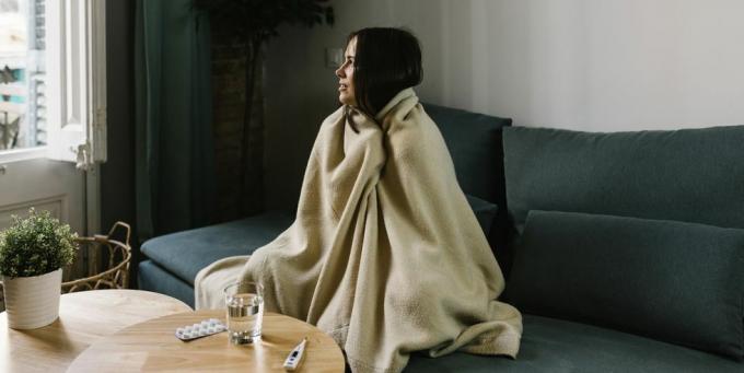 mulher doente olhando para longe enquanto enrolada em cobertor em casa