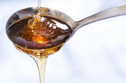 Uma garoa de xarope ou mel cai dentro e fora de uma colher.