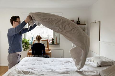 Homem fazendo cama enquanto mulher que trabalha na mesa no quarto