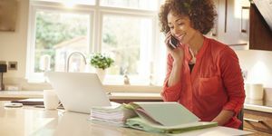 A mulher senta-se em sua cozinha e trabalha com alguns papéis enquanto conversa no telefone