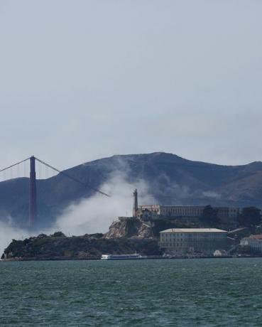 Uma névoa baixa gira em torno de Alcatraz e da ponte Golden Gate sob um céu claro enquanto os barcos navegam na baía de São Francisco