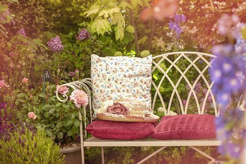 Uma bela cadeira de jardim em ferro fundido de verão com almofadas e um chapéu de verão, cena chique gasto