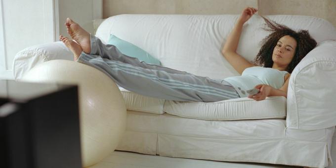 mulher deitada no sofá usando o controle remoto da televisão